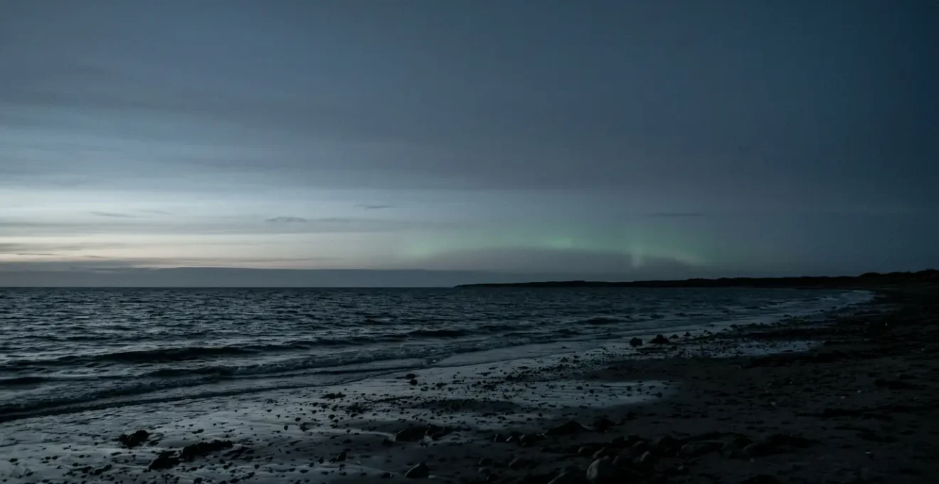 Faint aurora borealis glowing on the northern horizon over a dark Danish coastal landscape at twilight