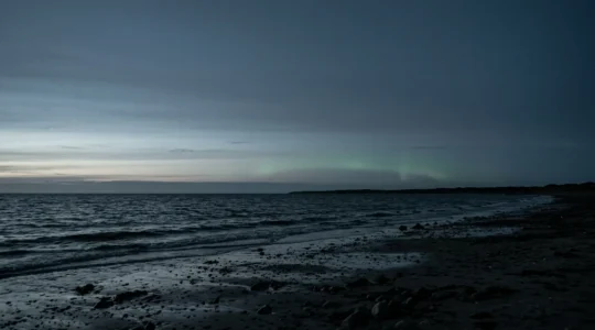 Faint aurora borealis glowing on the northern horizon over a dark Danish coastal landscape at twilight