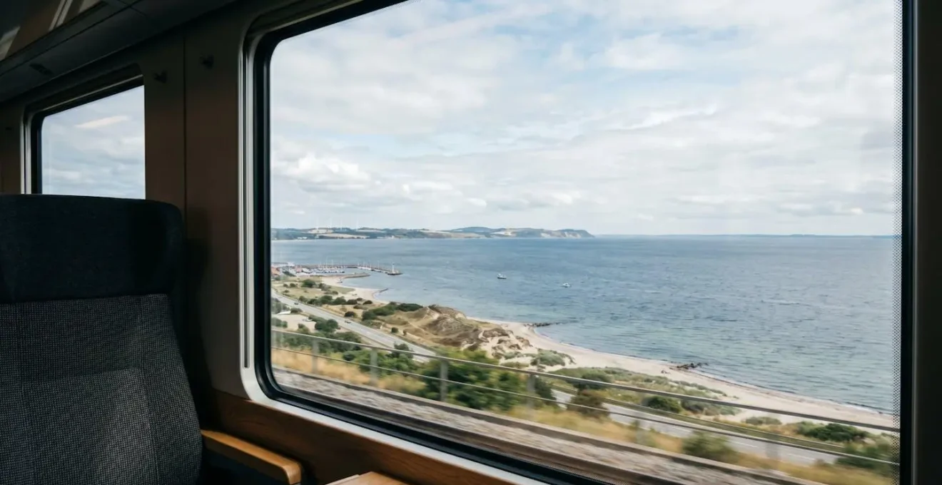 Passenger view from a Danish coastal train window overlooking the Øresund Strait with Sweden visible across the water