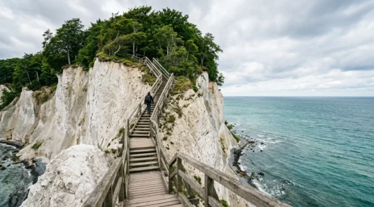 Hikers ascending dramatic wooden staircase along white chalk cliffs overlooking turquoise Baltic Sea