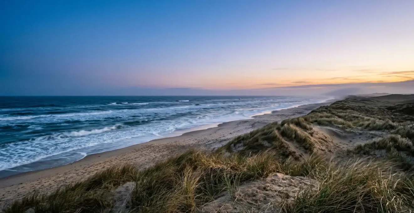Dramatic coastal landscape of Denmark with wild waves meeting golden sand dunes under evening blue hour light