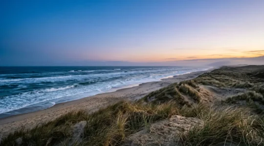 Dramatic coastal landscape of Denmark with wild waves meeting golden sand dunes under evening blue hour light