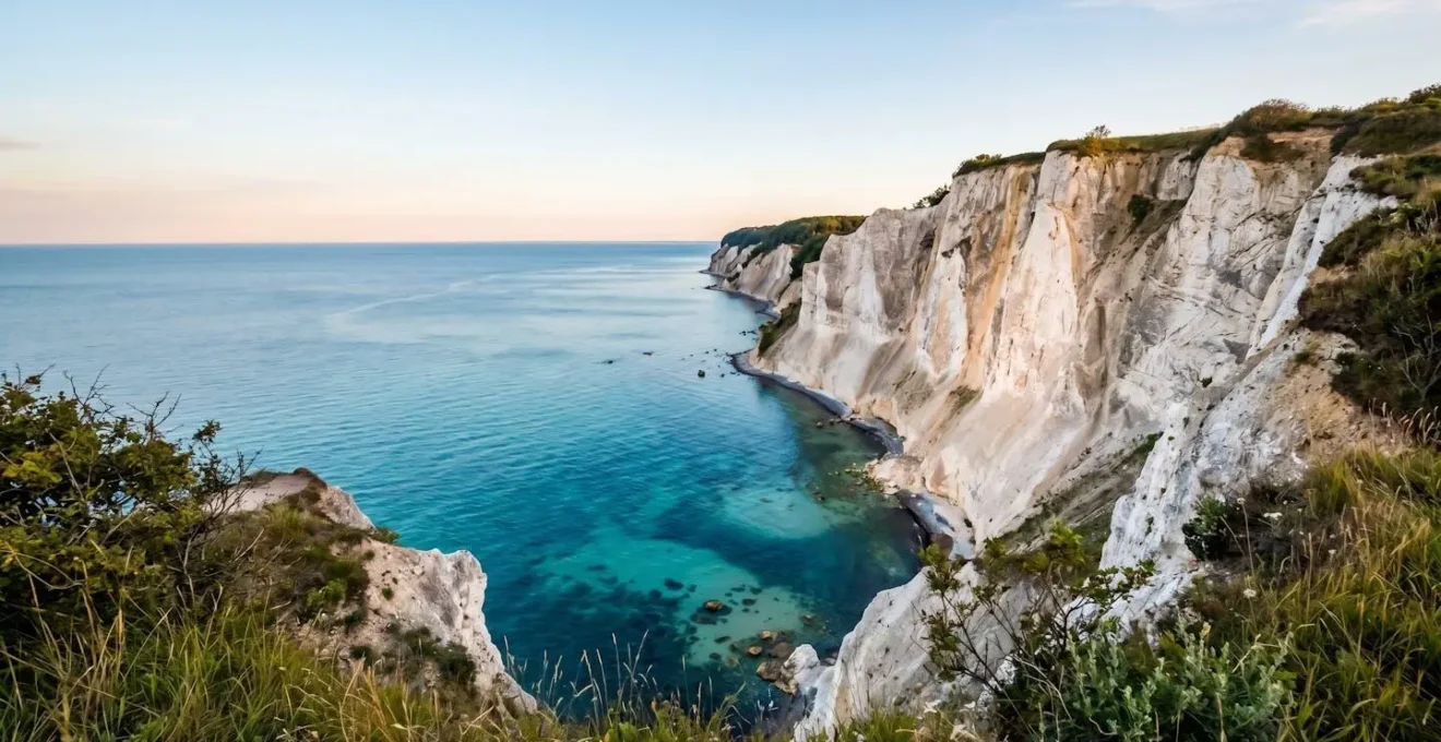 Wide-angle environmental shot of ethereal chalk cliffs meeting turquoise Baltic waters under Nordic sky