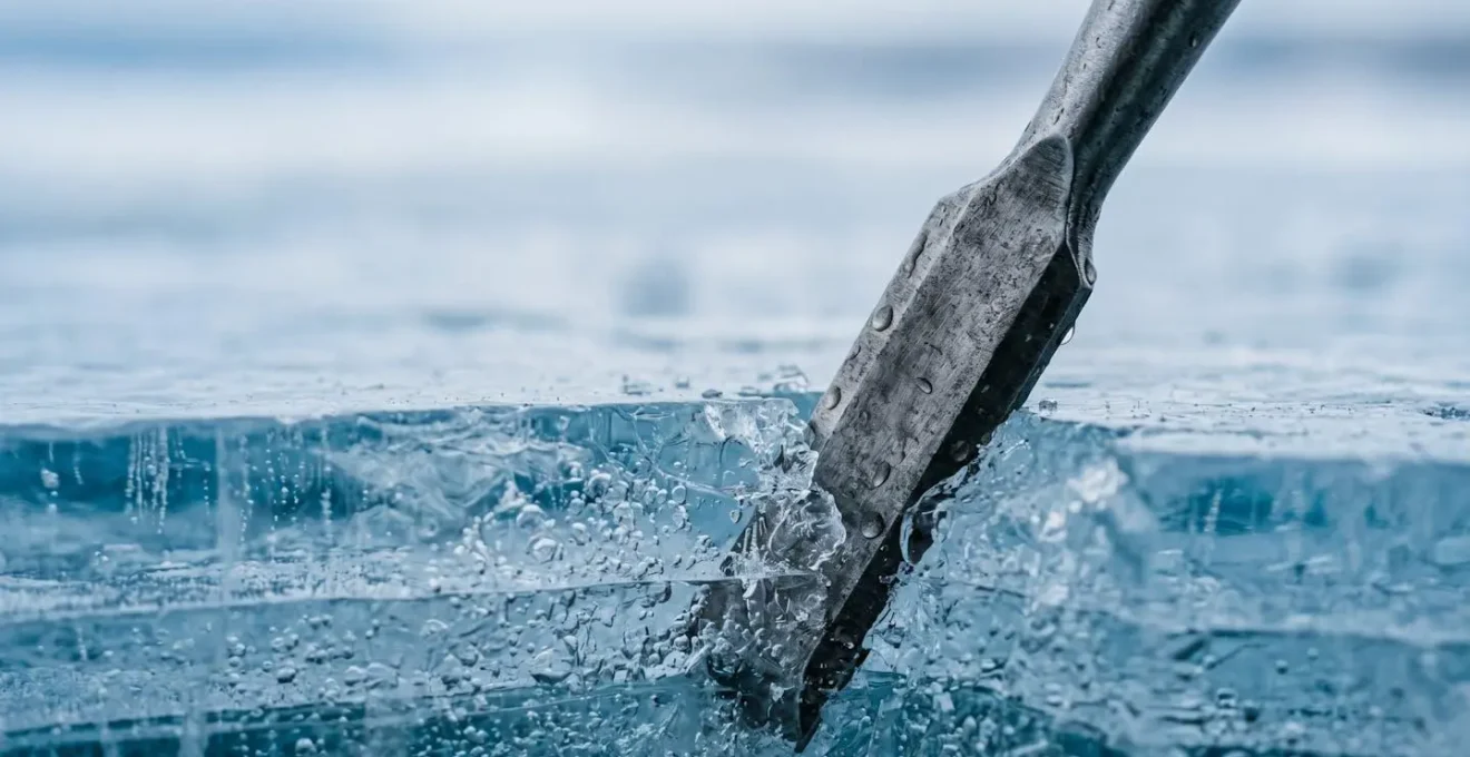 Macro close-up of ice chisel breaking through clear blue lake ice revealing ice thickness and crystalline structure