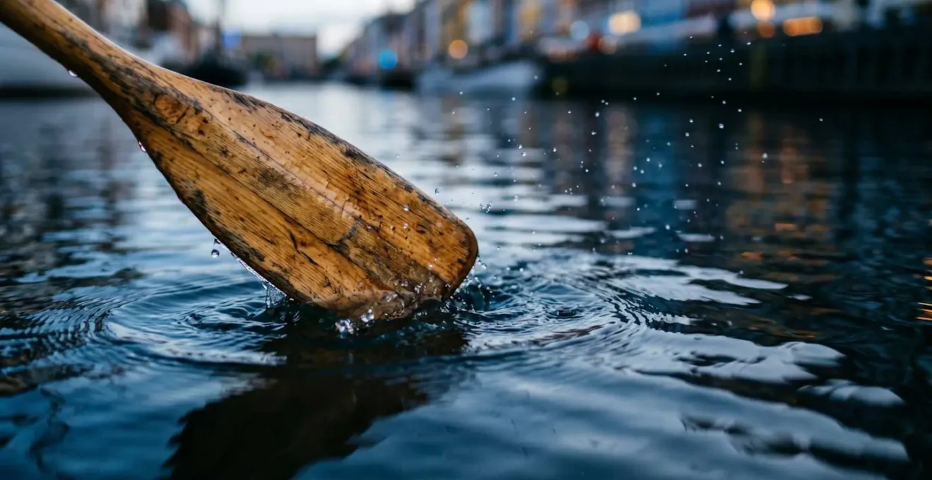 Close-up view of kayak paddle creating ripples in calm Copenhagen canal water during twilight with soft blue hour lighting