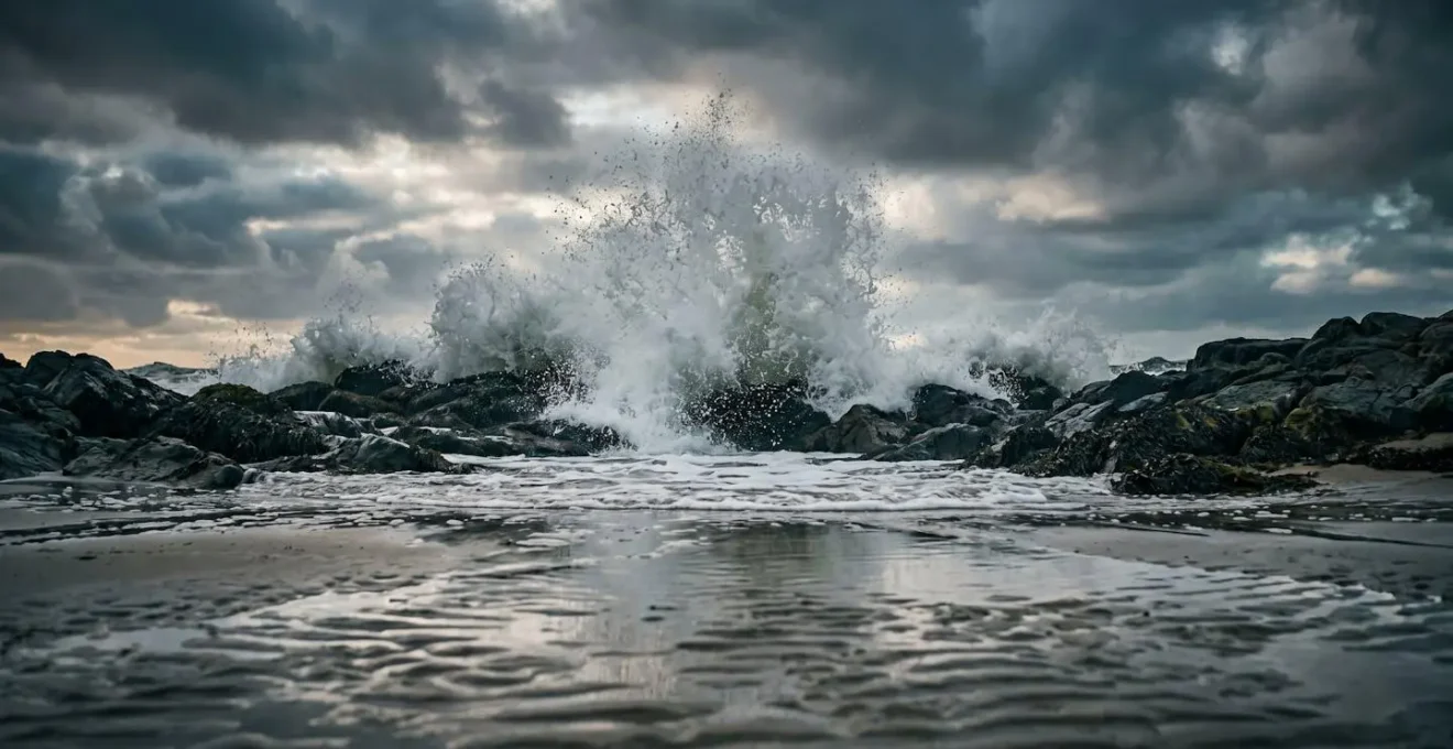 Powerful North Sea storm waves crashing against weathered coastal rocks under dramatic grey skies captured from photographer's low angle