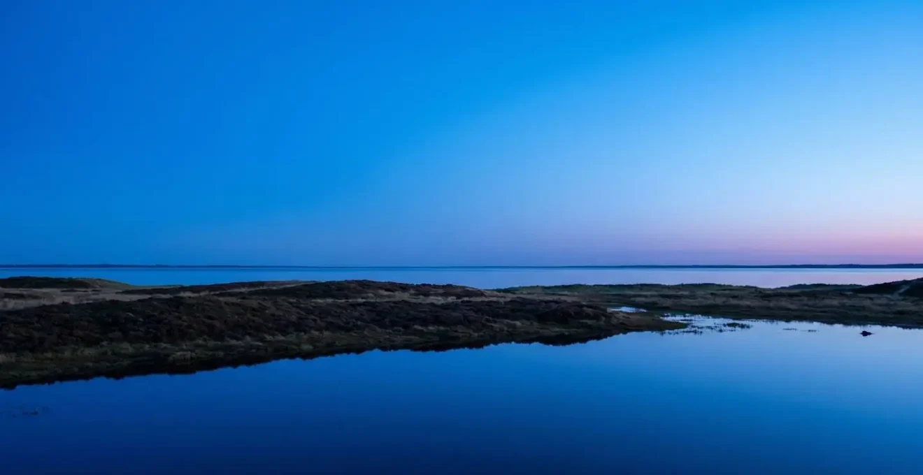 Deep blue twilight over Danish coastal landscape showing extended blue hour with saturated blue sky gradient and moody atmosphere