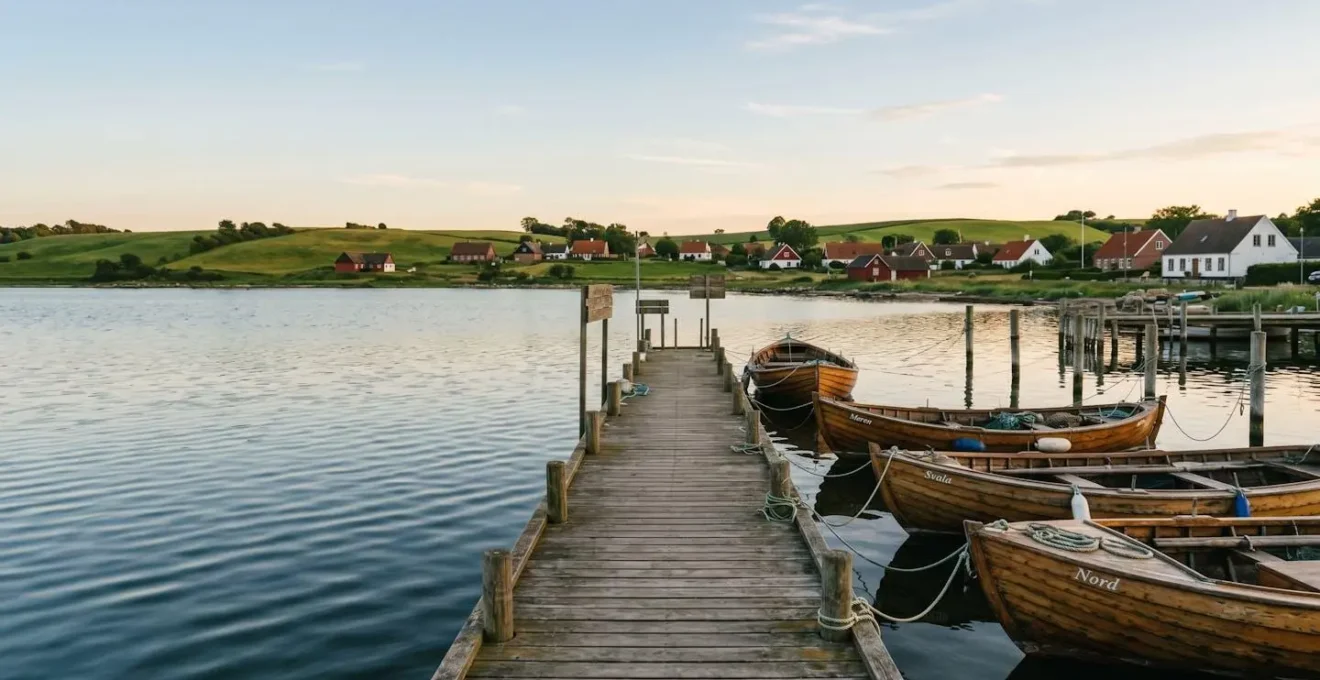Serene Danish archipelago harbor with wooden boats moored at a small island marina surrounded by green hills and traditional cottages